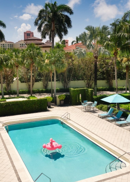 the private pool at Bungalows surrounded by beach chairs and palm trees. There is an inflatable pink flamingo floating the water